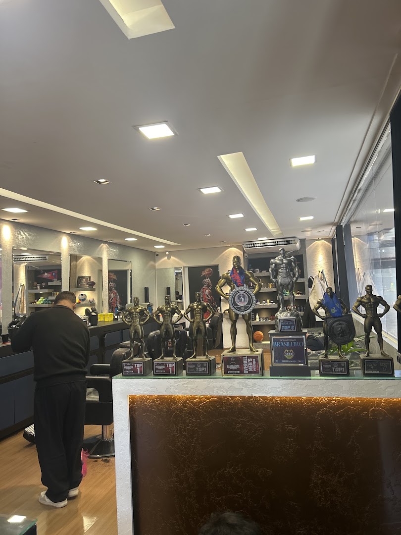 Barbeiro no balcão da USA Barber, com troféus expostos ao fundo